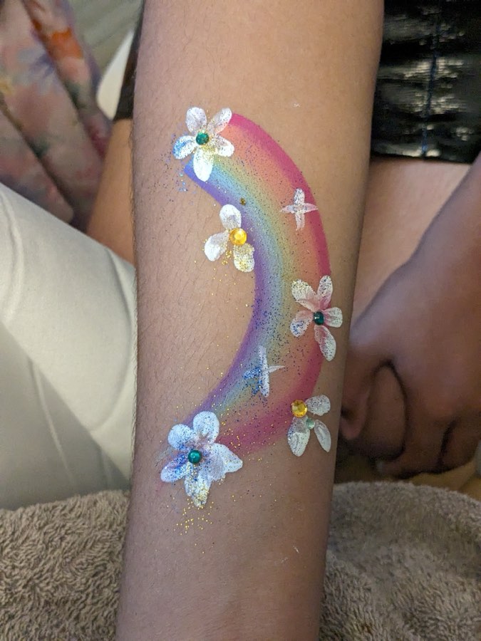 Rainbow glitter arm painting decorated with white flowers and gems