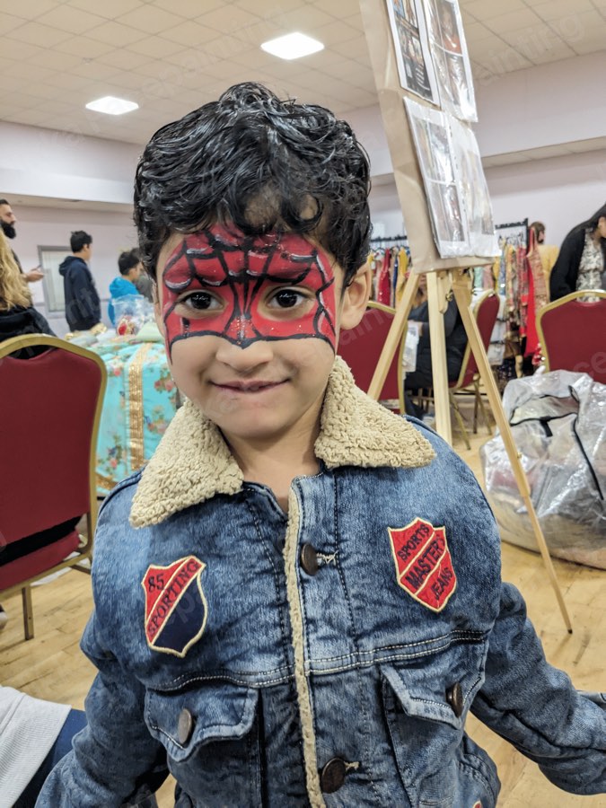 Child with a red spider hero mask face painting at an indoor event