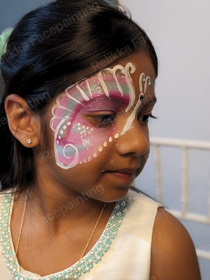 Child with a pink and white butterfly face painting with swirls and dots