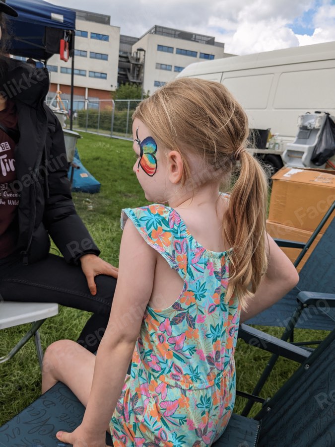 Little one at an outdoor fun day with a rainbow butterfly painted on the cheek
