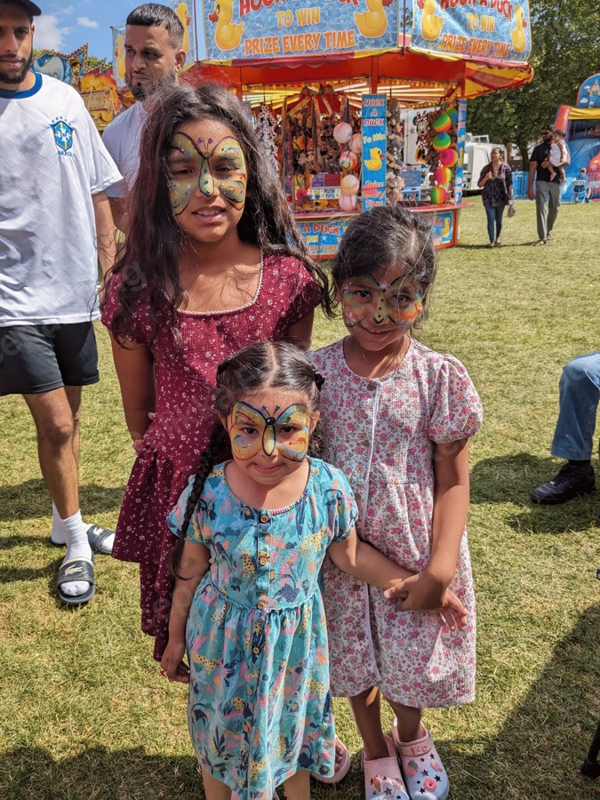 Three children with butterfly face paintings at a funfair