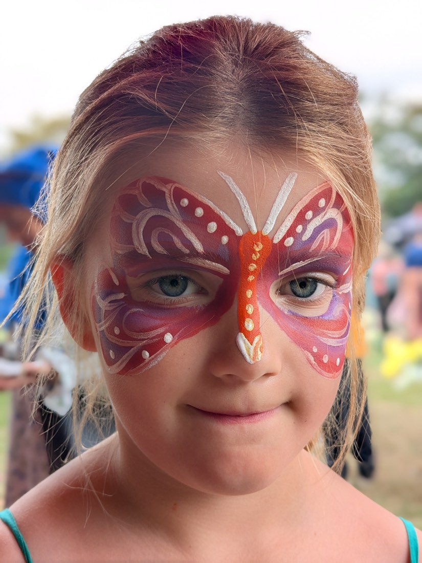 A smiling child with a red and pink butterfly mask face painting with white swirls