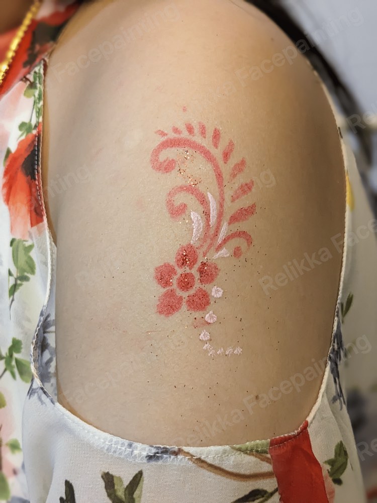 A red glitter tattoo of a flower with swirls on a child's arm